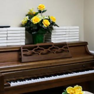 A wooden piano decorated with a vase of yellow roses and stacked books.