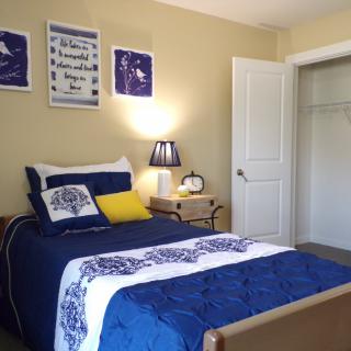 A cozy bedroom with blue-themed decor, featuring a single bed, nightstand, and open closet.