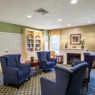 A cozy living room with blue armchairs arranged around a fireplace, featuring a bookshelf and elegant decor.