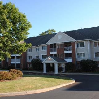 A three-story residential apartment building with a well-maintained landscape and trees, captured during the daytime.