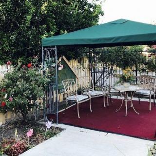 A cozy outdoor seating area under a green canopy, surrounded by trees and a charming picket fence.