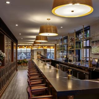 A modern bar interior with a long counter and elegant lighting.