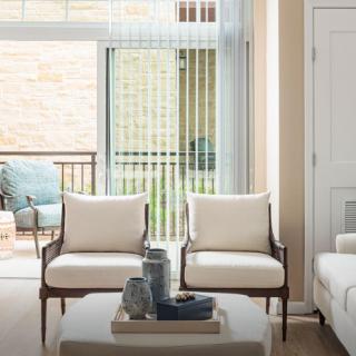 A modern living room featuring two armchairs and a coffee table near a large window with vertical blinds.