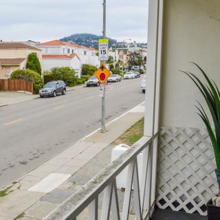 A view from a balcony overlooking a residential street with parked cars and houses.
