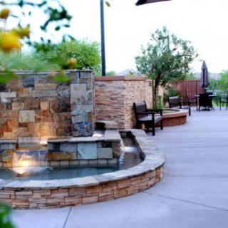 A peaceful patio with a stone fountain and outdoor seating, surrounded by lush greenery.