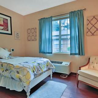A cozy bedroom with a single bed, blue curtains, and an armchair by the window.