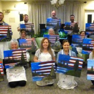 A group of people proudly displaying their completed landscape paintings in a class setting.
