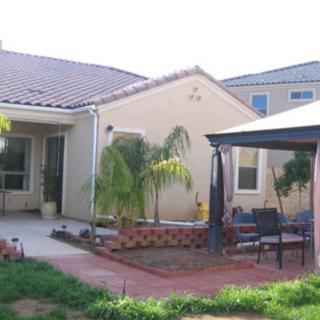 A cozy backyard with a patio and gazebo, featuring a small garden with palm trees.