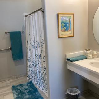 A clean and bright bathroom with turquoise accents, featuring a shower curtain, sink, mirror, and colorful towels.