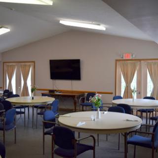 A spacious community meeting room with round tables and chairs arranged for gatherings.