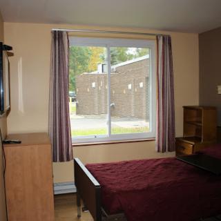 A cozy bedroom featuring a bed, TV, and large window with curtains.