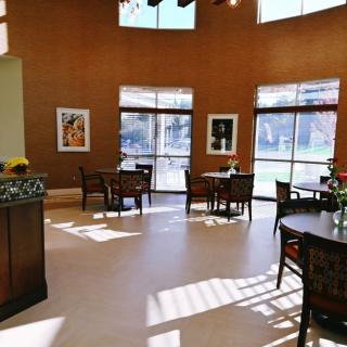 A cozy and bright cafe interior with several tables and chairs, adorned with artwork on the walls and large windows letting in natural light.