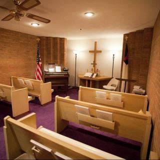 A small chapel with wooden pews, an altar with a cross, and an American flag displayed on one side.