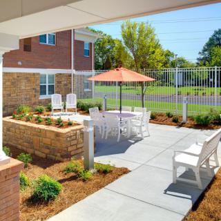 An inviting outdoor patio area with seating and an umbrella, surrounded by landscaped gardens.