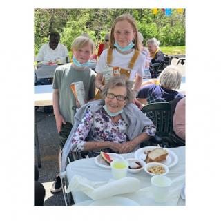 A family gathering outdoors with an elderly woman and children enjoying a meal together.