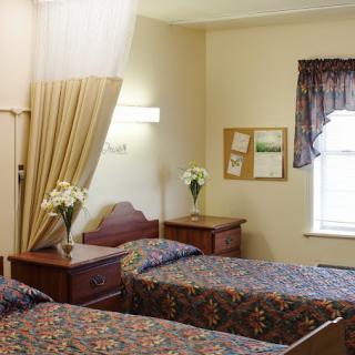 A cozy bedroom with two beds featuring floral bedspreads, nightstands, and a curtained window.