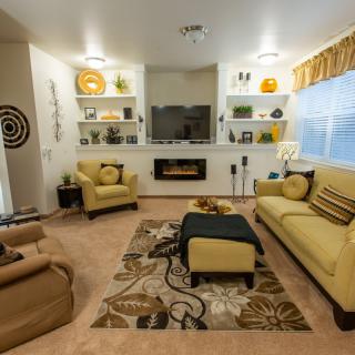 A modern, cozy living room with yellow and neutral tones, featuring a television, decorative shelves, and comfortable furniture.