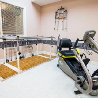 Rehabilitation room equipped with an exercise bike and parallel bars for physical therapy.