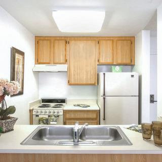 A compact kitchen with wooden cabinets, a stainless steel refrigerator, and a double sink.