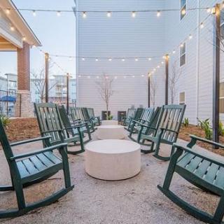 An inviting outdoor patio with a circle of rocking chairs around a fire pit, illuminated by overhead string lights.