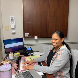 A person working at an office desk, smiling while using a computer.