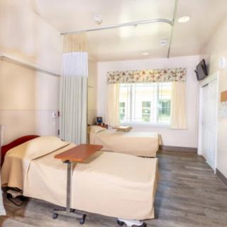 A hospital room with two beds, curtains for privacy, and a wall-mounted television.