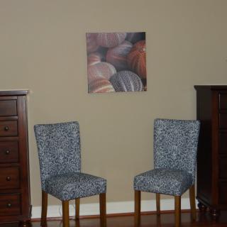 A room interior featuring two patterned chairs, a dresser on each side, and a piece of wall art.