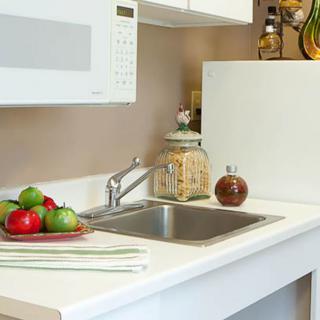 A clean kitchen counter with a sink, microwave, and apples on the countertop.