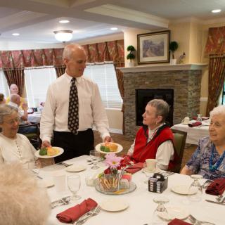 A server delivers meals to a group of elderly individuals dining together.