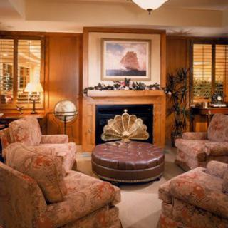 A cozy living room with plush armchairs, a central coffee table, and a decorative fireplace adorned with artwork and warm wood paneling.