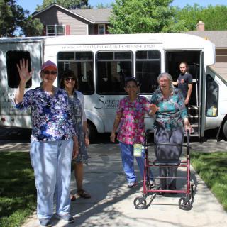 A group of seniors on an outing, standing in front of a minibus with one person using a walker.