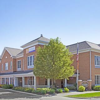 A brick building with a tree in front, a flagpole, and well-maintained landscaping.