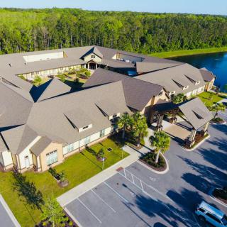 Aerial view of a large building complex surrounded by a parking lot, with a lake and lush greenery nearby.