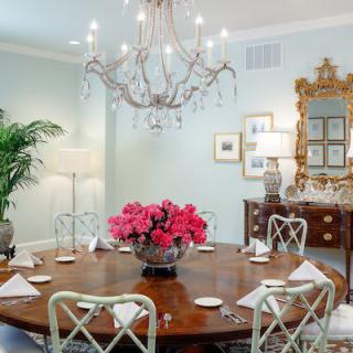 An elegant dining room with a chandelier and a round table featuring a floral centerpiece.