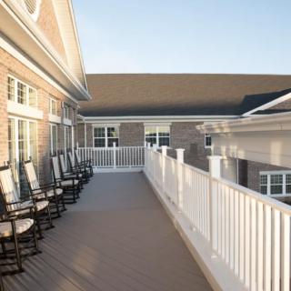 A spacious balcony with a row of rocking chairs and white railings, attached to a building.