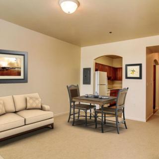 A modern living room with a dining area, featuring a sofa, dining table with chairs, and artwork on the walls. The kitchen can be seen in the background.