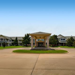 A wide driveway leading to the entrance of a large residential building, surrounded by well-maintained landscaping.