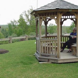 A person relaxing in a wooden gazebo surrounded by lush greenery.