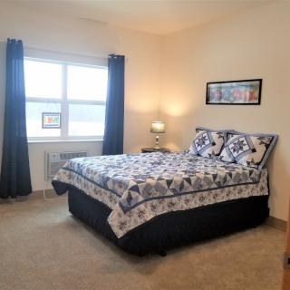 A cozy bedroom with a double bed, bedside lamp, and large window with curtains.