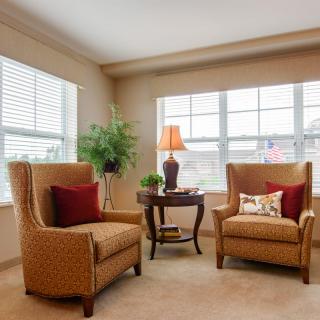 A cozy living room corner with two armchairs, a small table, and a lamp by the window.