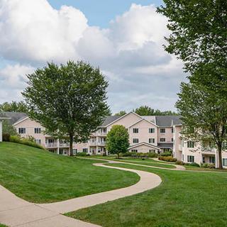 A scenic view of residential apartment buildings surrounded by lush green lawns and trees under a partly cloudy sky.