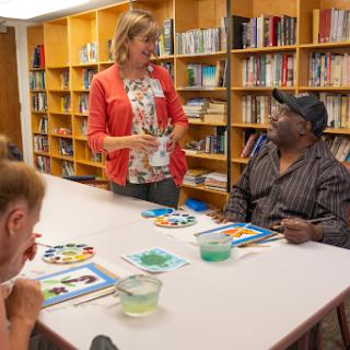 A vibrant art class taking place in a library, where participants engage with materials and interact with an instructor.