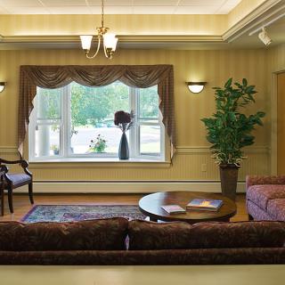 A cozy living room with elegant decor, featuring a sofa, coffee table, large window with curtains, and a potted plant.
