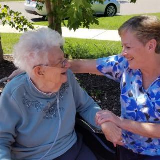 An elderly woman and a caregiver share a joyful moment outdoors.