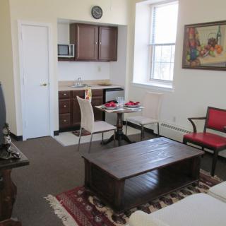 A cozy studio apartment featuring a small kitchen area, dining table with chairs, and comfortable seating.