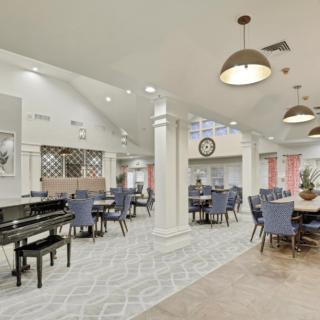 A spacious dining area with tables and chairs, featuring a piano and decorative lighting.
