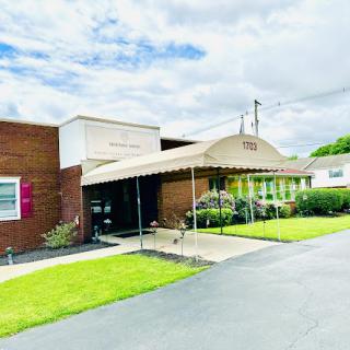 A modern building with a welcoming entrance, surrounded by lush green grass and a cloudy sky.