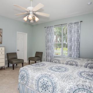 A cozy bedroom featuring twin beds with patterned bedding, a ceiling fan, and natural light coming through a window with curtains.
