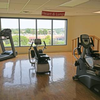 A bright gym room with exercise equipment including a treadmill and stationary bikes.