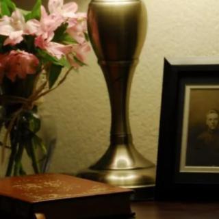 A cozy corner with a lamp, flowers, a photo frame, and a book on the table.